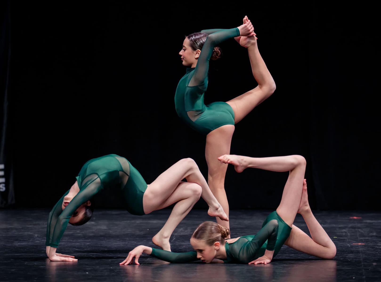 Three dancers in green costumes performing a contemporary dance pose on stage
