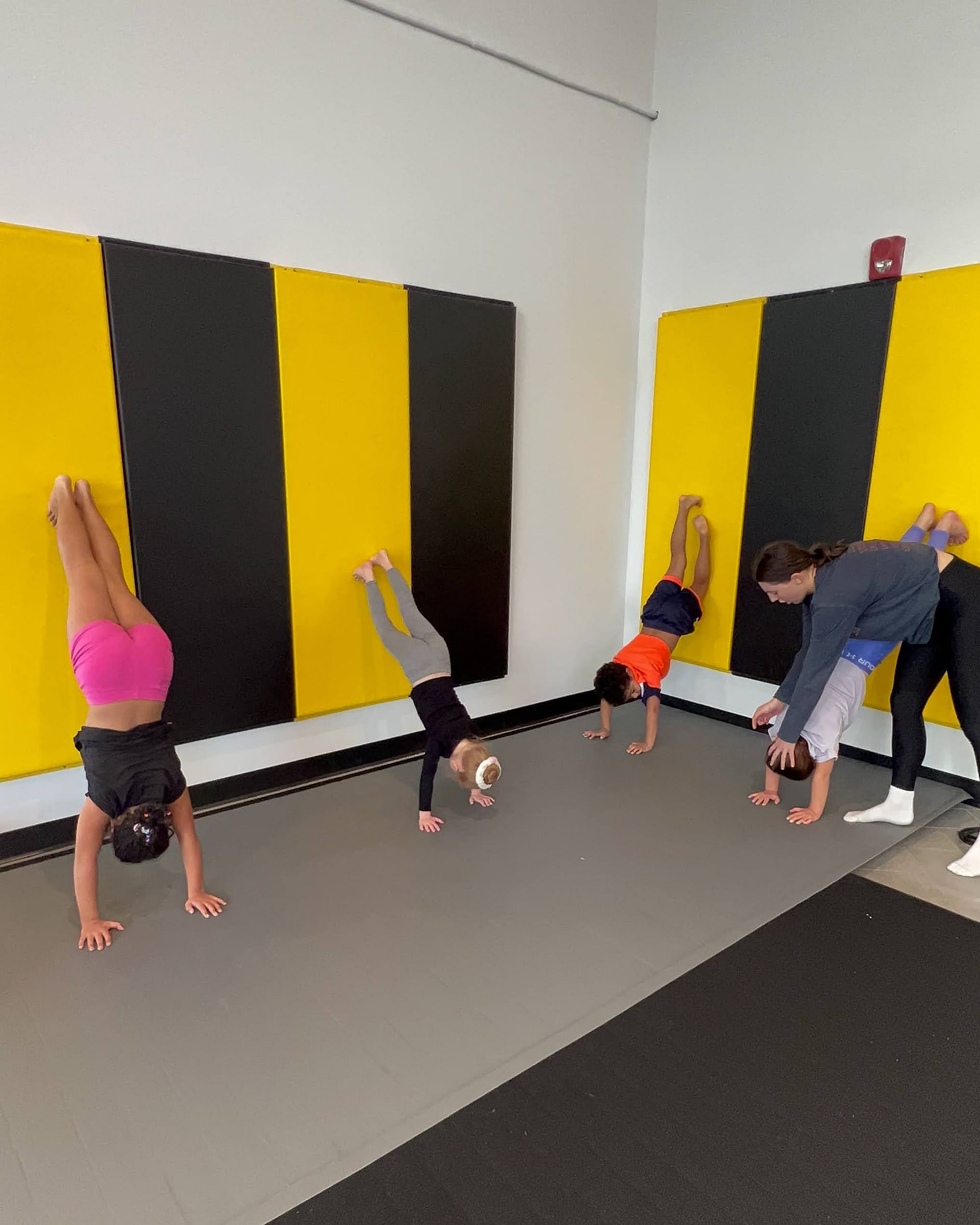 kids handstand against wall with teacher helping